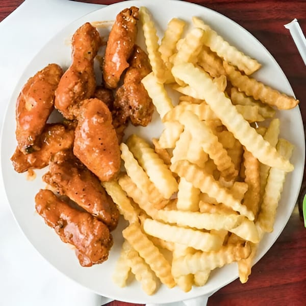 A white plate holds G Town Wings & Fish's saucy wings and crinkle-cut fries.