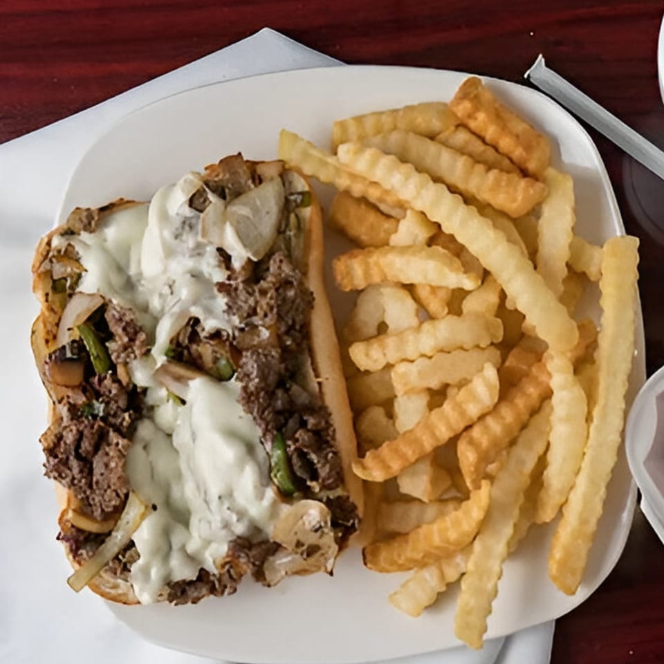 A G Town Wings & Fish cheesesteak sandwich with melted cheese, onions, and peppers, served with crinkle-cut fries.