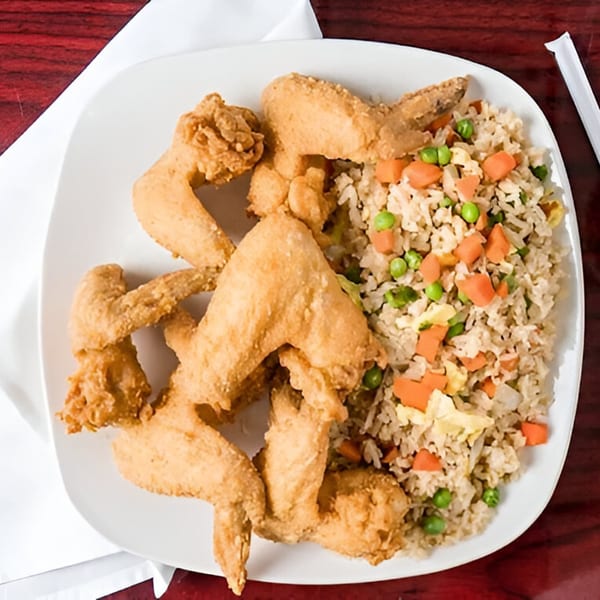 A white plate with crispy fried chicken wings and a side of vegetable fried rice.