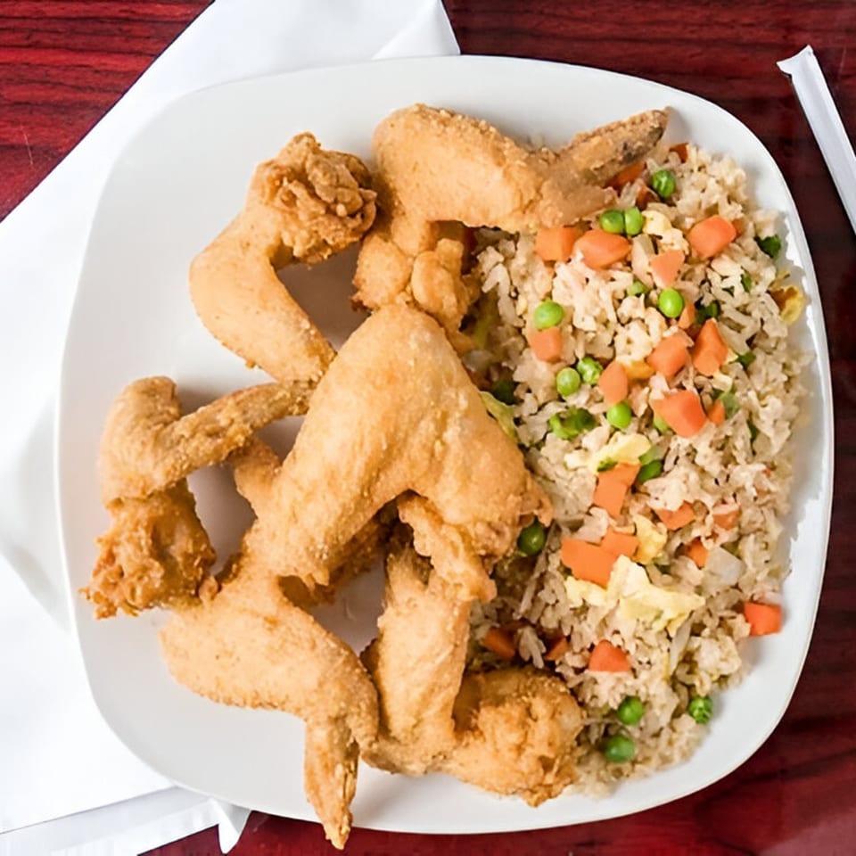 A white plate with crispy fried chicken wings and a side of vegetable fried rice.